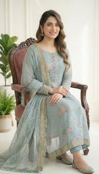 Woman in a light blue traditional outfit sitting on a wooden chair indoors.